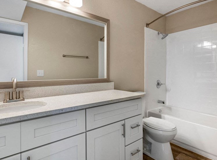 Bathrooms with hardwood style flooring, tiled showers, quartz countertops, framed mirror, white cabinets, and vanity lighting